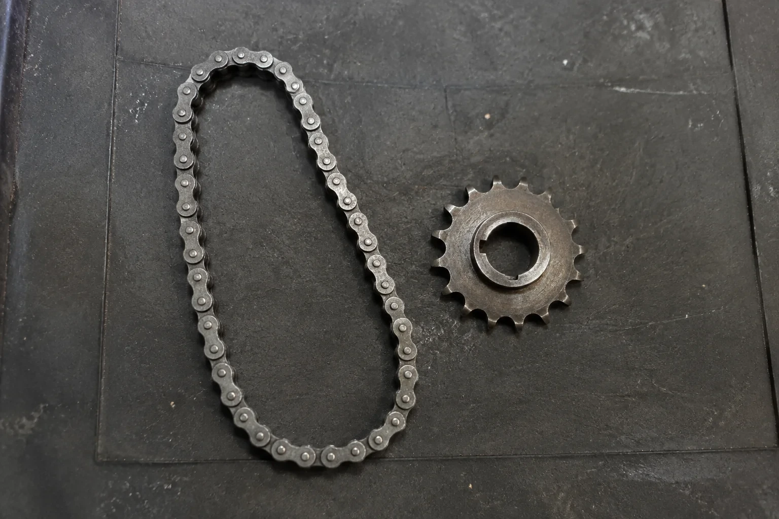 A short roller chain loop and separate sprocket on a dark work mat.