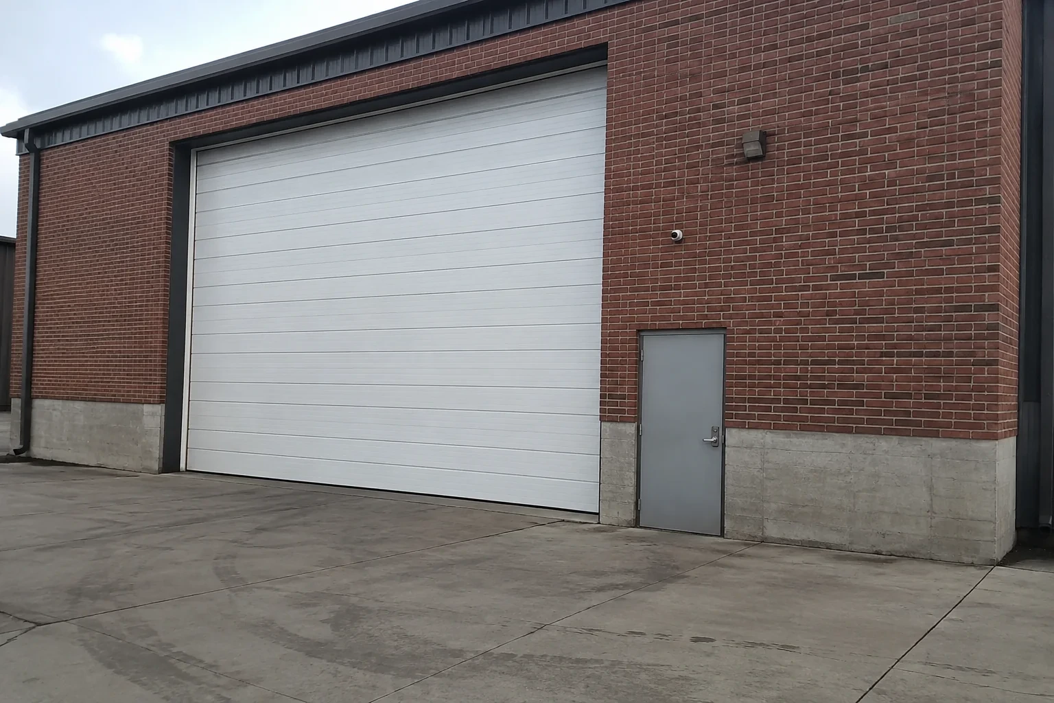Tall closed sectional loading door beside a personnel door at a brick unit.