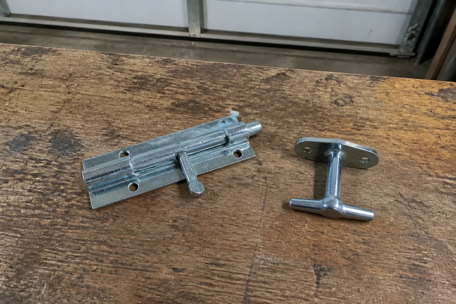 Detached slide bolt and T-handle on a wooden garage workbench.