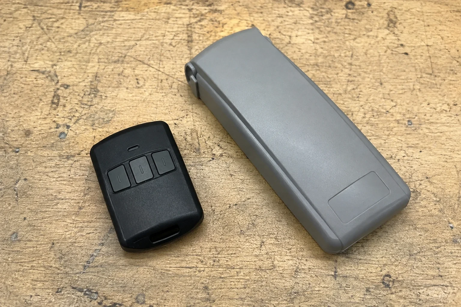 Three-button remote beside a closed grey keypad cover on a workbench.